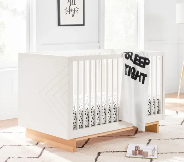 White BabyBliss Convertible Crib shown in a cozy nursery setting with soft pastel tones. The crib features a timeless design with slatted sides and a sturdy construction, offering versatility with its ability to convert from a crib to a toddler bed. Ideal for growing children, this crib blends classic style with modern functionality, creating a serene and safe sleep environment.