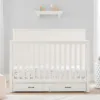 PureComfort 4-in-1 Convertible Storage Crib in a neutral wood finish, featuring built-in storage drawers and a sleek, modern design. The crib is staged in a cozy nursery setting with soft bedding and plush toys, showcasing its versatility and space-saving functionality.